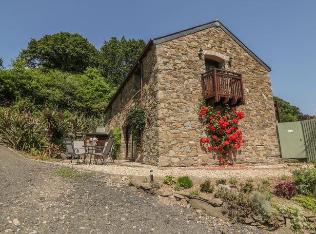 A stone house with a small balcony and red flowers outside with patio furniture at Bearscombe in Modbury