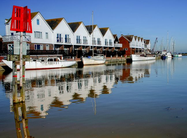 A row of white houses with peaked roofs and boats docked on calm water at 17 The Boathouse in Rye