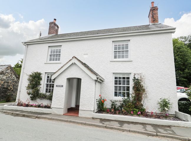 A white two-story house with a small porch and plants along the front at Llys Alaw in Llangernyw