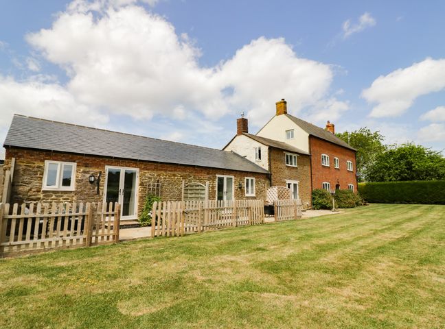 An exterior view of a stone and brick house with a wooden fence and a lawn at Ash Barn in Catesby