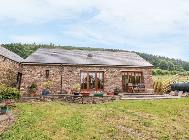 A stone house with wooden framed glass doors and potted plants on a stone patio in a grassy area at The Barn in Abergavenny