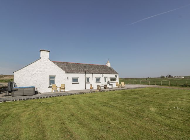 A white stone cottage with patio furniture and a hot tub on a lawn at Longforth Farm Cottage in Auchenmalg near Glenluce