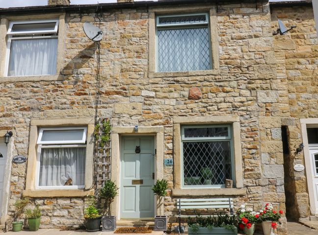 Stone cottage exterior with green door and windows with lattice design and plants in pots at Woodman Cottage in Skipton