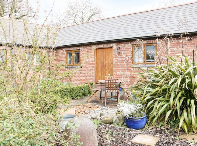 A garden area with plants and wooden chairs and table outside a brick building at Acorn Cottage 1 Burlton near Ellesmere