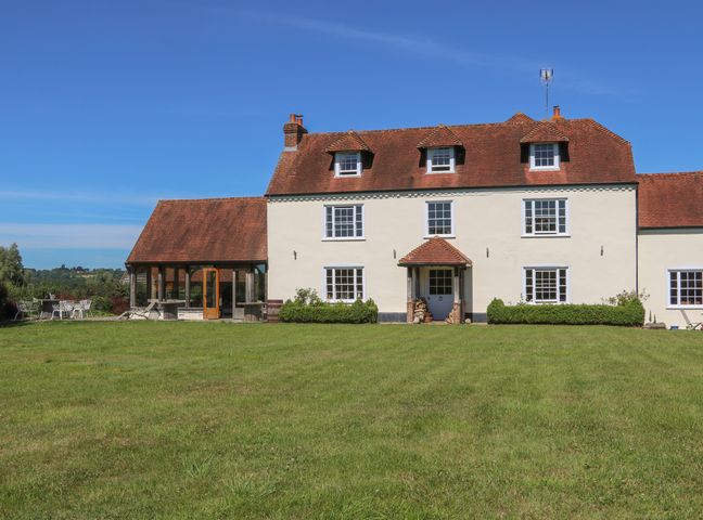 The exterior of a large house with white walls a red tiled roof and a green lawn at Groomes Country House in Farnham