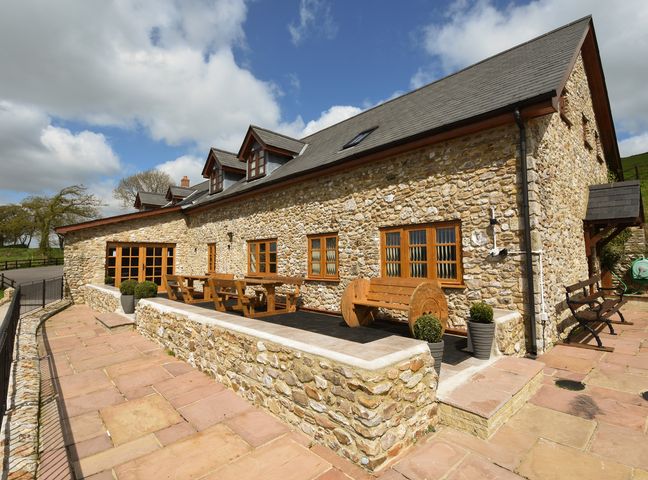 An outdoor patio with wooden benches and tables outside a stone house at The Barn Southleigh near Beer