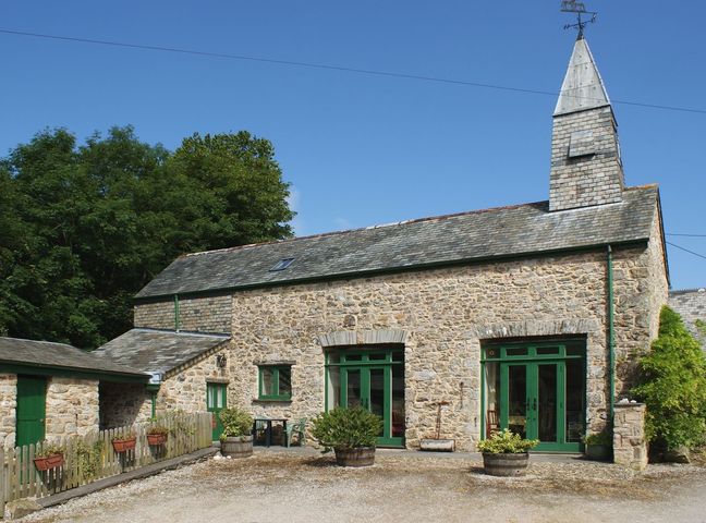 A stone building with green doors and windows and a small fenced garden area in front at The Clock House in Ivybridge