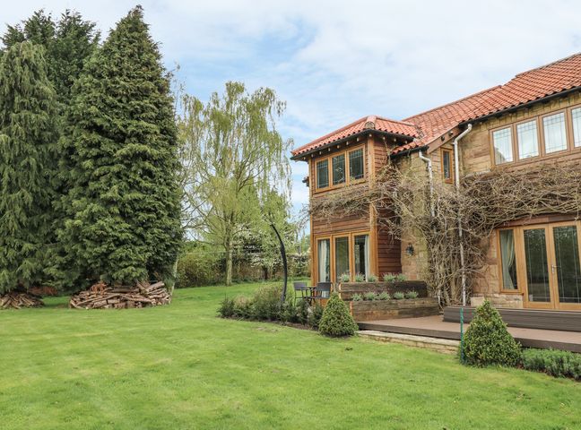 A garden with green grass and trees next to a house with a red tiled roof at Pond View in Cuckney