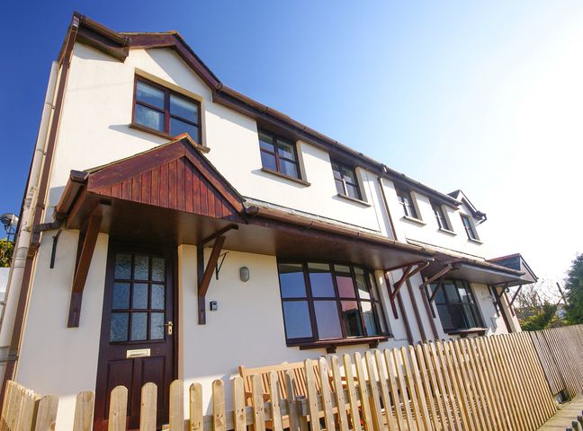 Exterior of a two-storey house with wooden door awnings and a wooden picket fence