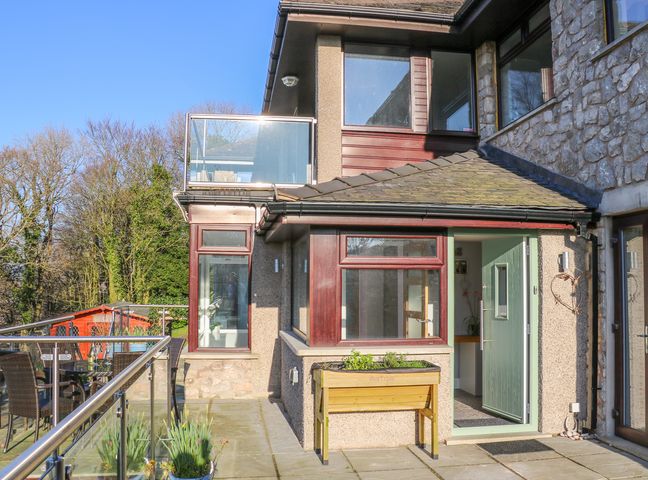 A patio with a glass railing table and chairs and a door leading inside a stone and pebble dash house at Shady Bowers in Arnside