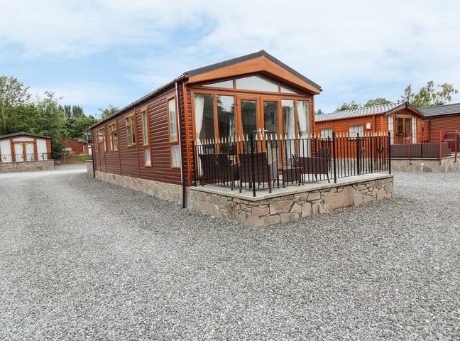 A gravel driveway with multiple wooden lodges and an outdoor seating area at 32 Cruachan Lodge in Auchterarder