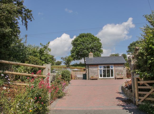A driveway with flowers and a wooden gate leading to a small house with a large window at The Boundary Annex in Bishop's Castle