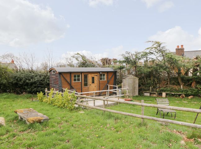 A wooden cabin with a fenced garden bench and trees at Railway Carriage in Govilon