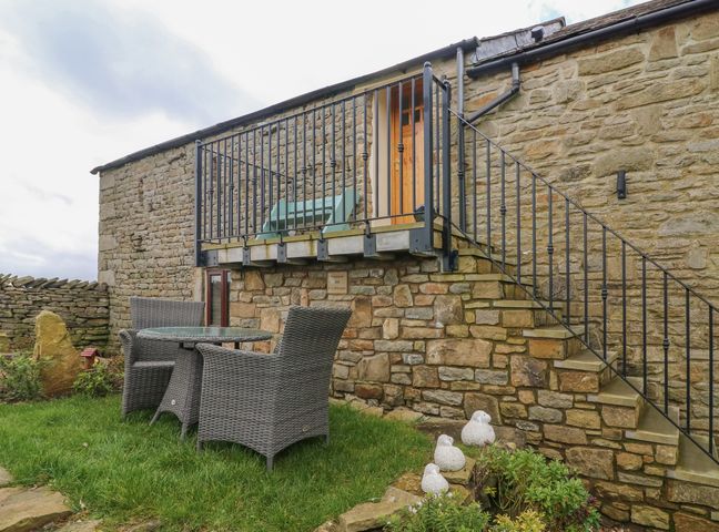 An outdoor stone patio area with wicker table and chairs next to stone stairs and railing at Melsome Barn Giggleswick near Settle