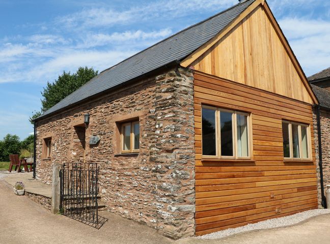 An exterior view of a stone and wood cottage with windows and a small gate at The Cottage in Treborough near Washford