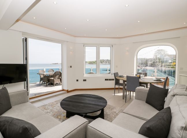 A living room with sofas a round coffee table dining table and chairs with a view of the sea at 1 Ocean Bay Swanage