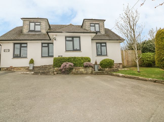 A white house with dormer windows and a driveway with shrubs and a tree at The Orchard in Crantock