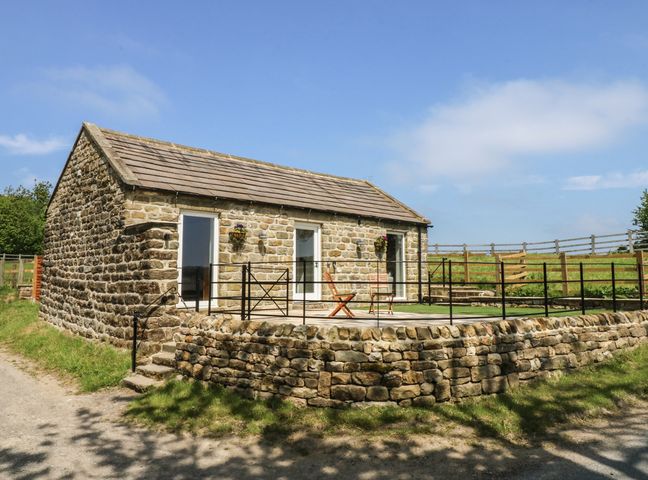A stone cottage with a raised patio and two wooden chairs surrounded by a metal railing at Lake Farm Cottage in Pateley Bridge