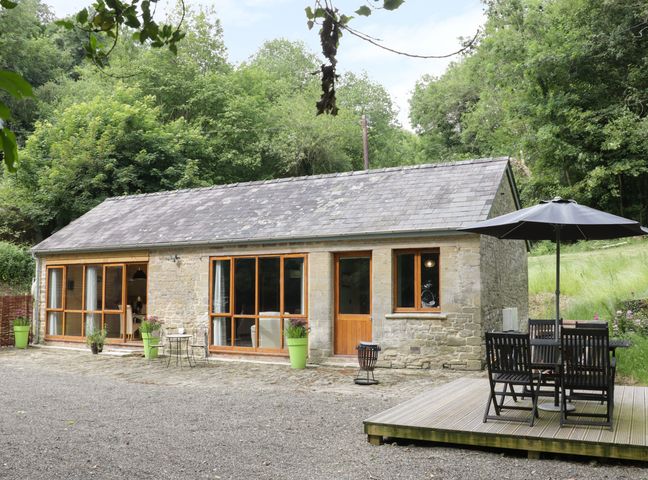 A stone cottage with wooden framed windows and door with patio furniture and umbrella outside at Woodpecker Cottage in Ludlow