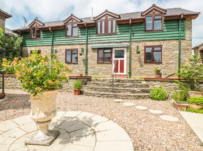 A stone house with green wood paneling and multiple windows with a garden featuring a large flower planter at The Courtyard in Gladestry