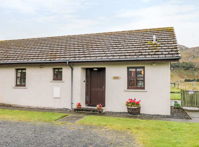 A single-story house with a tiled roof two windows a dark brown door and flower pots by the entrance at Church House in Poolewe