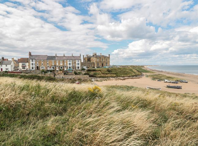 Houses and a large building near a beach with grassy dunes and boats at Larksbay View in Marske-by-the-Sea