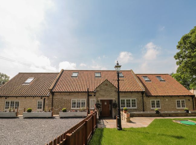 A stone house with a tiled roof and multiple windows a wooden fence and green grass at Ghyll Crest in Thirsk near Osmotherley