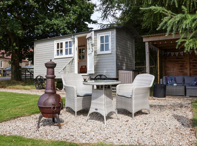 An outdoor seating area with a table and two chairs next to a small shed and a covered seating area at Bellwether in Helmsley