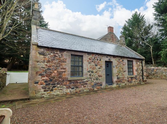 A stone cottage with a gray door and two windows surrounded by trees at Bracken Lodge in Wooler