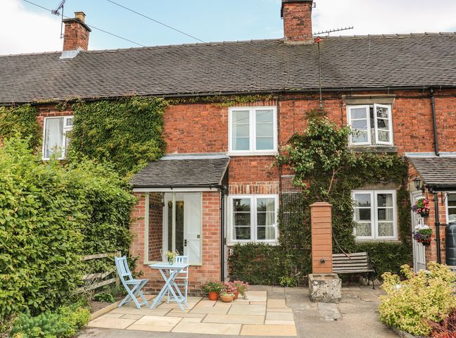 A brick cottage with ivy on the walls a small patio with a blue table and chairs and potted plants at Callow Cottages in Mappleton near Ashbourne