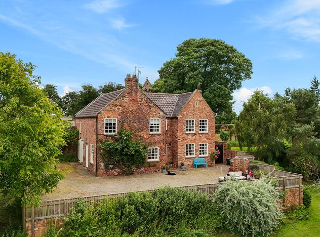 A brick house with multiple windows a blue bench and outdoor furniture in a fenced yard with trees at Manor Cottage in Northallerton