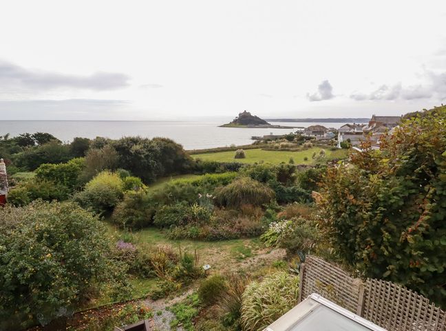 An outdoor view of a garden leading to the sea and an island at Greeb Rocks Cottage in Marazion