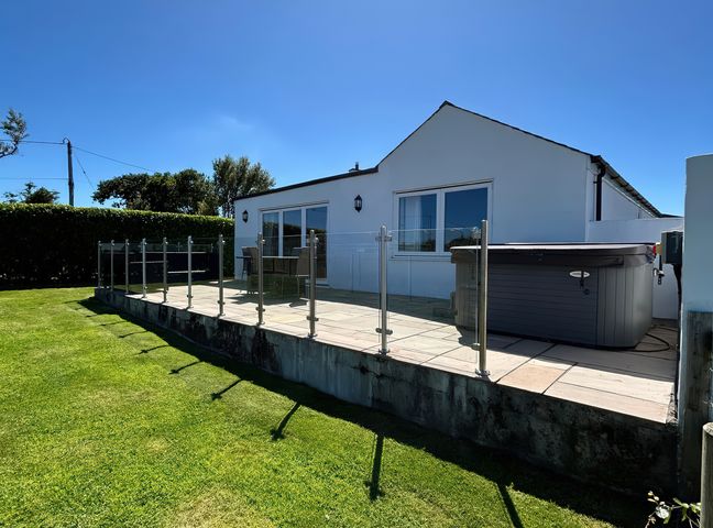 An outdoor patio with a hot tub and glass railing at Rhos Y Foel Cottage Nefyn
