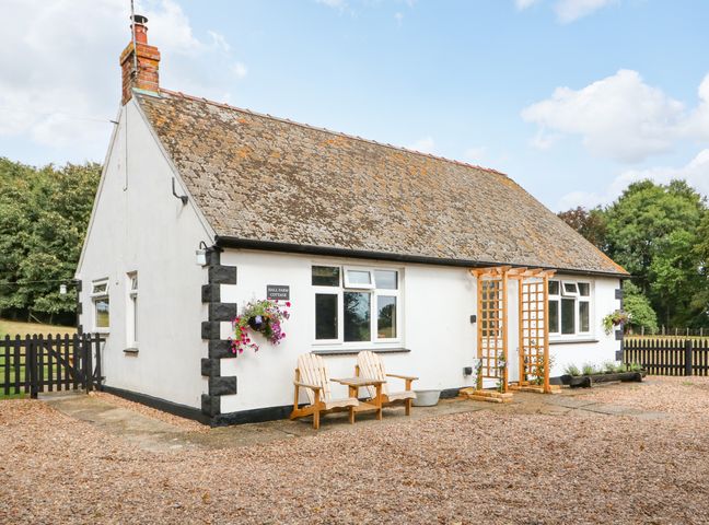 A white cottage with a tiled roof two wooden chairs and a small table outside at Hall Farm Cottage North Reston near Louth