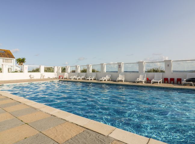 An outdoor swimming pool with lounge chairs around it at Fistral Surf in Newquay