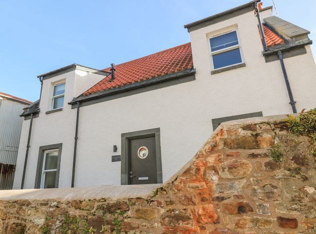 Exterior view of a white two-story house with red tiled roof and stone wall in front at Sandpipers in Crail