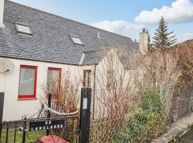 The exterior of a house with a slate roof and red window frames behind a wire fence at 25 Langlands Terrace in Kyle of Lochalsh