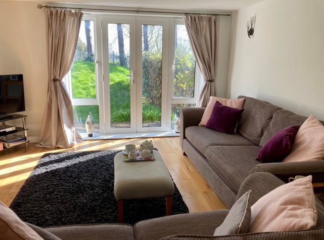 A living room with sofas and cushions near glass doors with curtains and a rug at Admirals Retreat in Weymouth