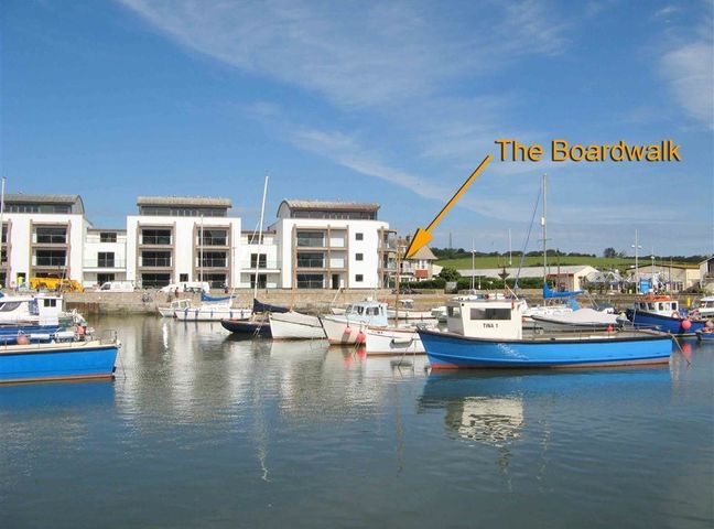 A harbor with boats docked and modern buildings in the background at The Boardwalk in West Bay