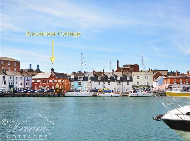 A waterfront with boats and buildings including Buccaneer Cottage at Brewers Quay Harbour