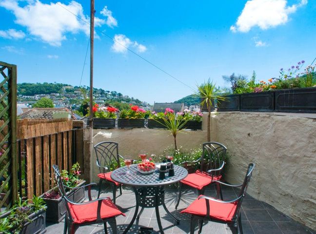 An outdoor patio with a round table and four chairs with red cushions at The Cottage 13 Clarence Hill Dartmouth