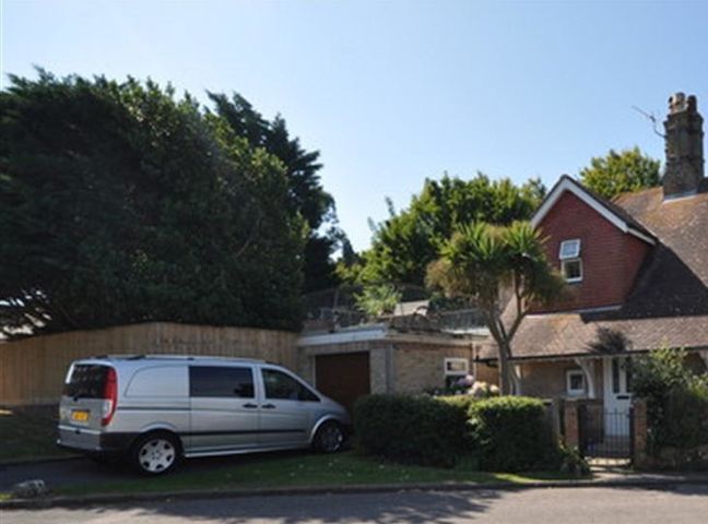 A driveway with a silver van parked next to a house with a garage and trees at Redcliff View Lodge in Weymouth