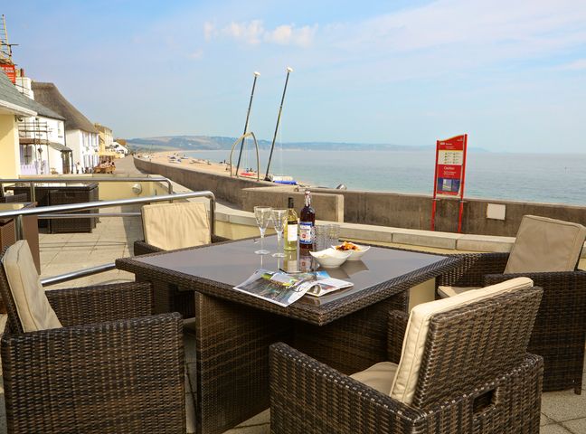 An outdoor patio with wicker chairs and a table set with drinks and snacks by the sea at 1 At The Beach in Torcross