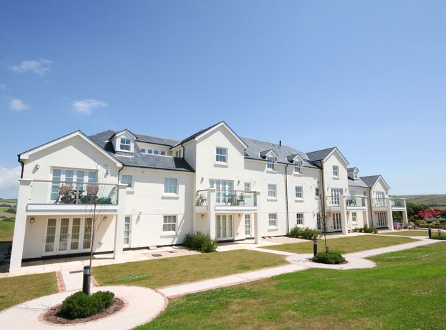 A white multi-unit building with balconies and glass railings overlooking a lawn with circular walkways at Horizon in Thurlestone