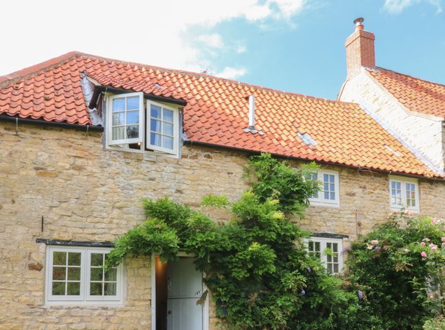 A stone cottage with a red tiled roof and white framed windows with green plants around at Kings Cottage in Fulbeck