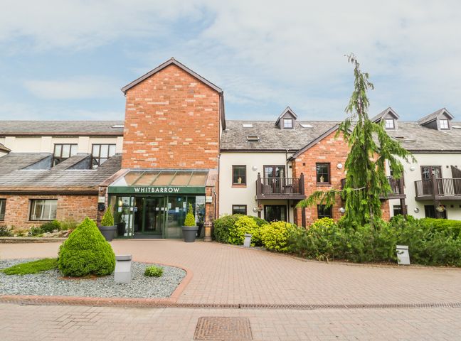 The entrance to a brick and stone building with a green sign reading Whitbarrow and landscaped greenery in front at Ullswater 29 in Penrith