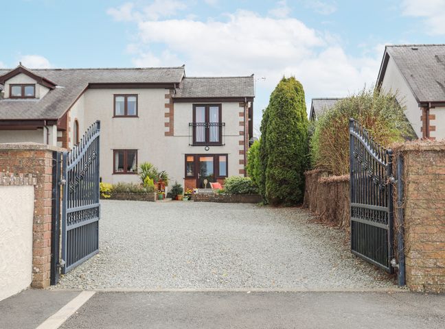 A driveway with open iron gates leading to a two-story house with plants at Bwlch Y Gwynt Bach in Llangefni