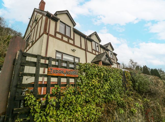 A two-story Tudor style house with a black wooden fence and ivy in front of it at Tudor House in Symonds Yat