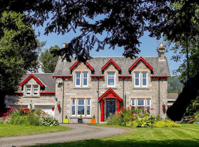 A stone house with red trim and a garden in front at Roseburn in Pitlochry