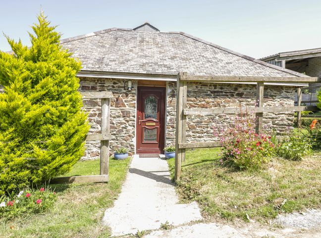Exterior view of a stone building with a red door a pathway leading to the entrance and plants on both sides at Garras Barn in Truro